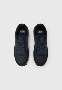 Paari mustad Diesel tossud paeltega, võrgu- ja seemisnahast detailidega, asetatud kõrvuti heledale taustale.