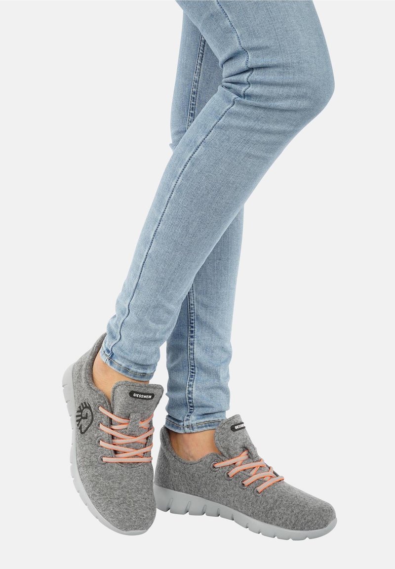 Chaussures en feutre grises avec des semelles en caoutchouc gris clair et des lacets pêche, avec un patch logo sur la languette et un design de bout arrondi.