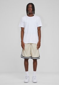 Hvid bomulds T-shirt parret med beige mesh shorts, der har sorte striber langs kanten. Båret med hvide sneakers og ankelsokker.