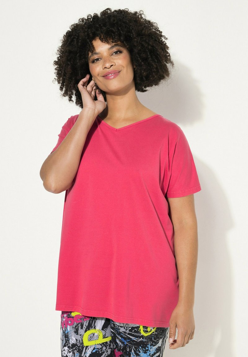 Rosa V-Ausschnitt-T-Shirt aus weichem Stoff, mit kurzen Ärmeln, lockerer Passform und glatter Textur. Gemusterte Hose im Bild sichtbar.
