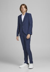 Marineblauwe pak met een getailleerde blazer en rechte broek, gecombineerd met een wit overhemd en witte sneakers. Op maat gemaakt ontwerp, zachte textuur.