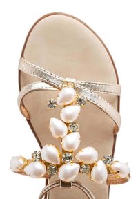 Sandalia beige con tiras metálicas doradas, adornada con perlas y cristales dispuestos en una forma floral. Suela blanda con textura suave.