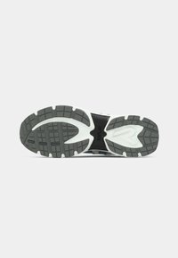 Semelle de chaussure avec une surface noire texturée, motif de semelle en caoutchouc gris et accents blancs. Éléments de design circulaires et linéaires visibles.