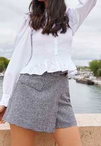 Top bianco con maniche a sbuffo, corpino arricciato e orlo a volants, abbinato a pantaloni corti a vita alta in check gessato bianco e nero con tasche laterali.