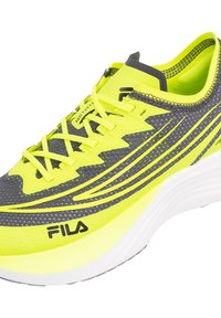 Zapatilla deportiva con parte superior de malla gris, acentos en amarillo neón y una entresuela blanca plana. Presenta cordones con costuras cruzadas y el logo de Fila en el lado.