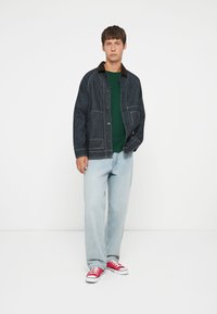Striped, blue denim jacket with brown collar, paired with a green sweater and light blue jeans. Red sneakers complete the outfit.