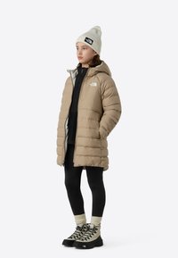 Beežist täispuhutud jope kapuutsi ja tõmblukuga, kantud üle musta pluusi ja retuuside. Tarvikuteks on kreemikas nokamüts ja mustad matkasaapad.