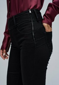 Jeans negros de mezclilla, con cintura alta, cierre lateral con cremallera y bolsillos frontales con un acabado texturizado.