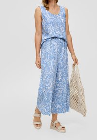 Modrý vzorovaný bezrukávový top a široké kalhoty vyrobené z lehkého materiálu. Spárované s tkanou taškou a platformovými sandály.