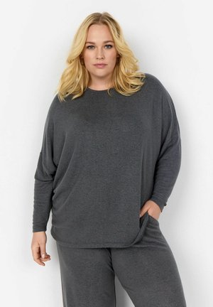 Haut de lounge gris avec des manches longues et une coupe décontractée. Le tissu a une texture douce et il y a un détail de poche sur le côté des pantalons.