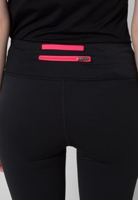 Leggings neri con vita alta, dotati di una tasca orizzontale con zip rosa e un piccolo etichetta di tessuto rosa sul retro.