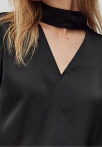 Top nero con scollatura a V e colletto. Il tessuto appare liscio, con un design minimale e una lieve lucentezza.
