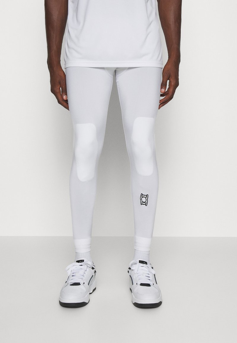 Leggings atletici bianchi con accenti imbottiti sulle ginocchia, texture liscia e un piccolo logo nero vicino alla caviglia. Abbinati a sneakers bianche.