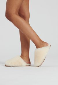 Crème kleurige fluffy pantoffels met een zachte textuur, een open achterkant en een duurzame zool, die een eenvoudige en gezellige uitstraling laten zien.