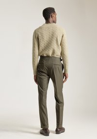 Suéter de punto trenzado en beige claro, combinado con pantalones oscuros verdes a medida y con bolsillos traseros. Capturado desde atrás, mostrando la textura y el ajuste.