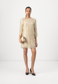 Beige klänning med en texturerad blommönster, trekvartsärmar och lös passform. Matchad med en liten beige handväska och svarta klackar.