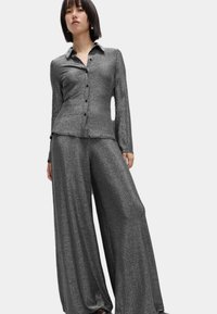 Skinnende sort to-delt sæt bestående af en knap-op langærmet skjorte og brede bukser, begge i et blødt, tekstureret stof.