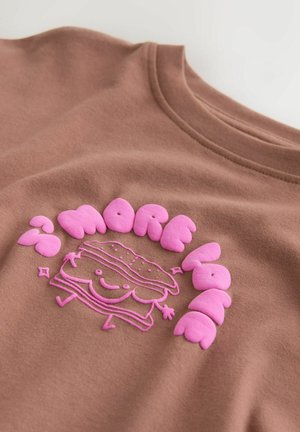 Braunes Baumwoll-T-Shirt mit einem rosa, reliefartig gedruckten Design eines lächelnden Sandwichs und dem Text "MORE" in geschwungenen Buchstaben darum.
