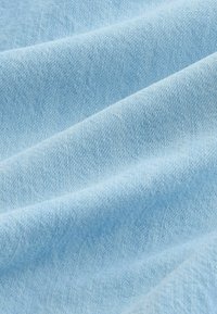 Tissu bleu clair avec une texture de tissage fin visible et des plis doux créant des ombres et des reflets délicats.