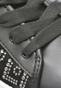 Sneaker nera in pelle testurizzata e suede, con lacci neri, occhielli in metallo e strass decorativi sul lato.