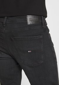 Jeans de mezclilla negra con una etiqueta de cuero en la cinturilla y un pequeño logotipo en el bolsillo trasero. Presenta un clásico diseño de cinco bolsillos.