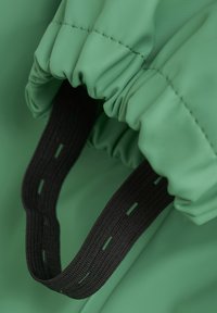 Grüner wasserdichter Stoff mit gerafften Kanten, einer weichen Textur und einem schwarzen elastischen Gurt mit Ausschnitten für sicheren Halt.