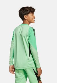 Maglia da allenamento verde con maniche lunghe, dotata di dettagli neri sulle spalle. Realizzata in materiale leggero, progettata per l'abbigliamento sportivo.