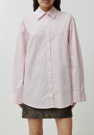 Helle rosa Hemdbluse mit klassischen Kragen, langen Ärmeln und lockerer Passform, kombiniert mit einem dunkel strukturierten Rock.