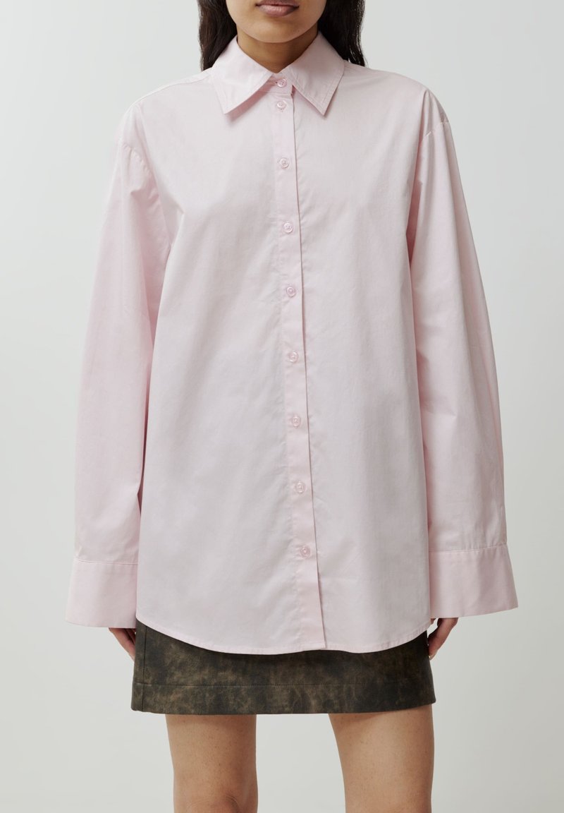 Helle rosa Hemdbluse mit klassischen Kragen, langen Ärmeln und lockerer Passform, kombiniert mit einem dunkel strukturierten Rock.