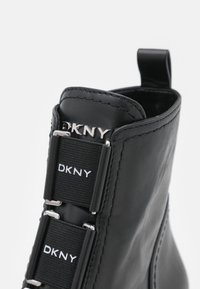 Černé kožené boty s elastickými pásky a DKNY brandováním, stříbrnými akcenty a poutkem na zadní straně pro snadné obouvání.