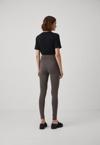 Camisola preta de manga curta combinada com leggings cinzas de cintura alta e lisa. Modelo usa sandálias de plataforma pretas, vista de trás.