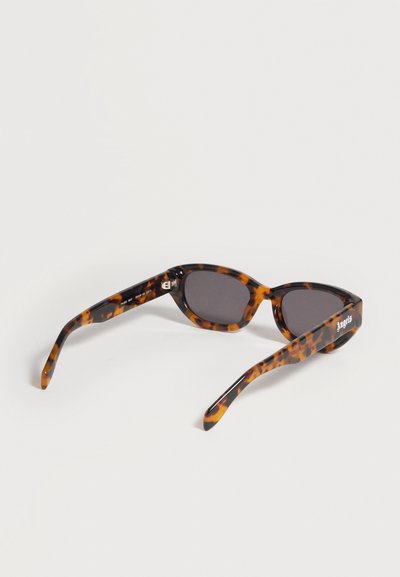 Lunettes de soleil rectangulaires à motif écaille de tortue avec verres foncés et inscription "Angels" sur la branche, exposées sur une surface blanche.