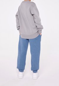 Felpa grigia con scollo rotondo e texture morbida, abbinata a pantaloni della tuta blu a vestibilità ampia. Entrambi i capi presentano tasche.