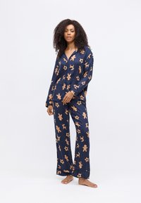 Marineblauw pyjama set met gingerbread- en rendiergewrichten, gemaakt van zachte stof. Het shirt heeft een knoopsluiting met lange mouwen en de broek heeft een relaxed fit.