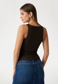 Brown ribbed tank top with a fitted design, paired with a blue denim skirt. Smooth texture and round neckline, showcasing a simple style.