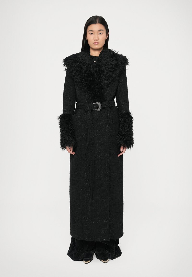 Črni dolg plašč iz teksturirane tkanine z ovratnikom in manšetami iz umetnega krzna. Pas z bleščečo sponko, vključeni stranski žepi.