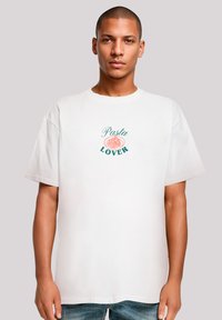 Witte katoenen T-shirt met een bedrukte graphic met de tekst "Pasta Lover" en een pastakom ontwerp in roze en groen. Korte mouwen, relaxte pasvorm.