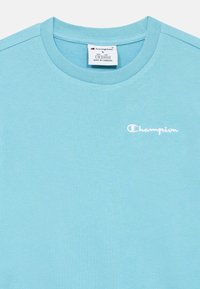 Τυρκουάζ κοντομάνικη μπλούζα από βαμβάκι, με λευκό κεντημένο λογότυπο «Champion» στο στήθος, λεία υφή και στρογγυλή λαιμόκοψη.