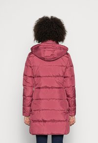 Chaqueta acolchada en color rosa con capucha, con costuras horizontales, mangas largas y un espalda ligeramente más larga. Tejido suave y brillante.