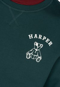 Sudadera verde oscuro con un gráfico blanco de un oso y el nombre "HARPER" en letras blancas arriba. Presenta un cuello de canalé y costuras visibles.