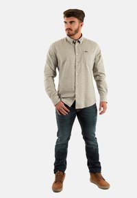 Lichtgrijze button-up shirt met een zak, gecombineerd met donkere spijkerbroeken en tan-kleurige schoenen. Het shirt heeft een subtiele uitstraling en een kraag.
