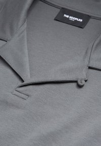 Polo gris avec un col plié et une étiquette noire portant la mention "THE KOOPLES PARIS" cousue à l'intérieur de l'encolure.