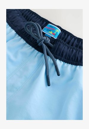 Lichtblauwe zwemboxers met een donkere tailleband, voorzien van een trekkoord en een "NEXT" merklabel met een kleurrijk strandontwerp.
