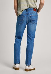 Bleknade blå jeans i denim med smal passform, med en brun läderplatta vid midjan och två bakfickor, matchade med vita sneakers.