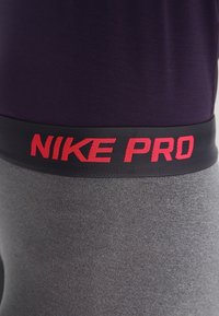 Nike Pro Sportbekleidung mit einem dunkelvioletten Oberteil und grauen Leggings. Verfügt über einen schwarzen elastischen Bund mit rotem "NIKE PRO" Schriftzug.