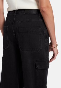 Pantaloni cargo in denim nero con vita alta, due tasche posteriori e una tasca laterale, dal tessuto liscio e dal design minimalista.