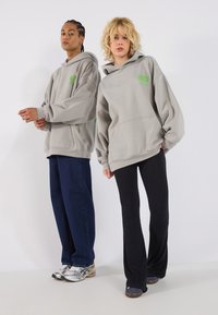Grå hettegensere med store lommer og grønne logoer, kombinert med mørkeblå vide denimbukser og svarte ribbede bukser, med ulike skomodeller.