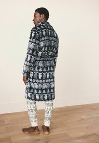 Rochie de noapte bleumarin cu un model alb de animale și fulgi de zăpadă, textură moale, cu talie cu brâu, asortată cu colanți crem cu modele similare.