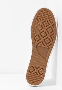 Semelle de chaussure en caoutchouc marron avec motif de bande de roulement géométrique comprenant des losanges, des croix et des lignes horizontales sur fond blanc.
