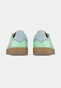 Πράσινα και γαλάζια αθλητικά παπούτσια με λεία υφή, χαρακτηριστικό κυματιστό τακούνι, ταμπά λαστιχένια σόλα και μίνιμαλ σχεδιασμό.